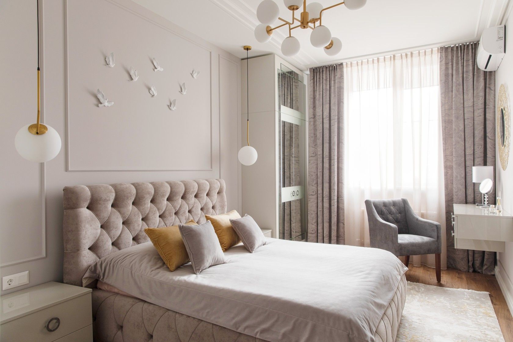 Modern bedroom with taupe tufted headboard, mustard and grey cushions, bird wall sculptures, and gold globe chandelier
